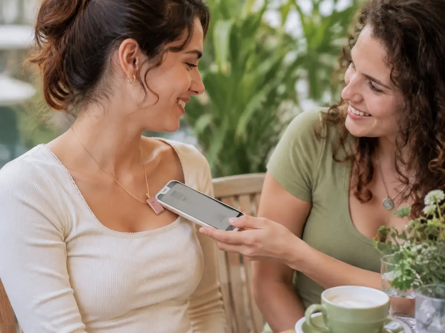 Two friends using a phone with a coral ceramic HavenTap pendant